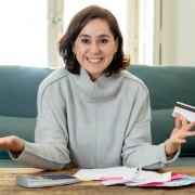 Young attractive latin business woman with credit card and calculator accounting costs, charges, taxes and mortgage on sofa at home paying bills looking happy and relaxed with own business success