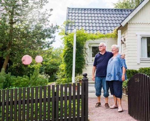 Ouder koppel staat gearmd voor hun woning, symbool voor kredieten hergroeperen na uw 50ste