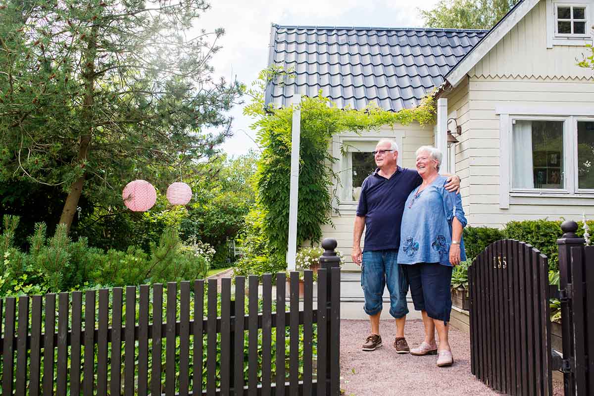 Ouder koppel staat gearmd voor hun woning, symbool voor kredieten hergroeperen na uw 50ste