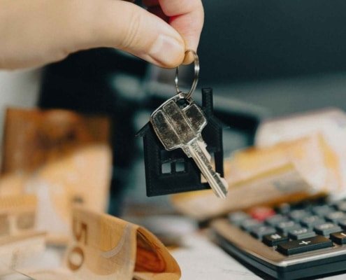 Sleutel met huisvormige hanger naast een rekenmachine en geld, symbool voor variabele hypotheekrente die fors is gestegen