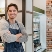 Zelfstandige ondernemer met gekruiste armen in zijn eigen winkel, symbool voor hypotheek hergroeperen als zelfstandige